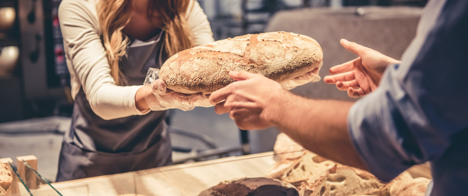Eine Verkäuferin reicht einem Kunden ein frisch gebackenes Brot über die Theke.